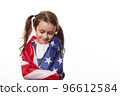 Close-up of delightful little girl with two cute ponytails, hugs herself, covered on United States of America flag, on independence day, isolated over white background, with space for your advertising 96612584