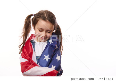 Close-up of delightful little girl with two cute ponytails, hugs herself, covered on United States of America flag, on independence day, isolated over white background, with space for your advertising Close-up of delightful little girl with two cute ponytails, hugs herself, covered on United States of America flag, on independence day, isolated over white background, with space for your advertising 96612584