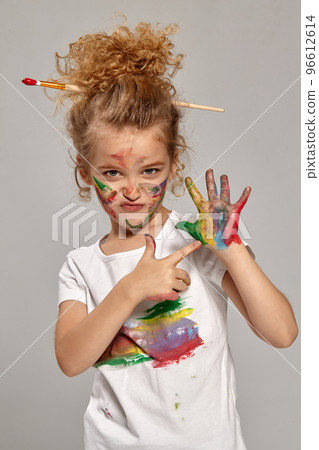 Beautiful little girl with a painted hands and cheeks is posing on a gray background. Beautiful little girl with a painted hands and cheeks is posing on a gray background. 96612614
