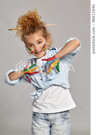 Beautiful little girl with a painted hands and cheeks is posing on a gray background. 96612640