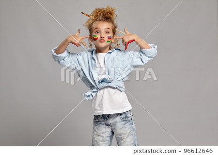 Beautiful little girl with a painted hands and cheeks is posing on a gray background. Beautiful little girl with a painted hands and cheeks is posing on a gray background. 96612646