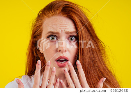 ungroomed nervous unhappy young redhaired ginger woman looking at a broken fingernail and crying .nude manicure in studio yellow background.dry and split ends of hair 96612688