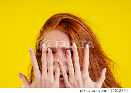 ungroomed nervous unhappy young redhaired ginger woman looking at a broken fingernail and crying .nude manicure in studio yellow background.dry and split ends of hair 96612894