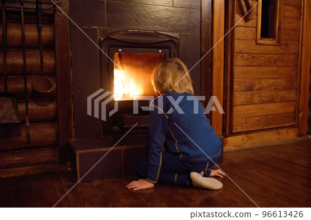 Little child is warming himself by the fireplace after a walk in cold weather in a village house. Preschool boy looks at the flame by the fire place. Little child is warming himself by the fireplace after a walk in cold weather in a village house. Preschool boy looks at the flame by the fire place. 96613426
