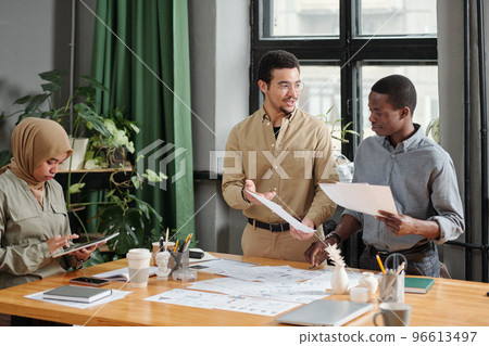 Two young businessmen discussing papers while their colleague using tablet 96613497