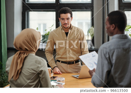 Young serious manager listening to report of Muslim female subordinate 96613500
