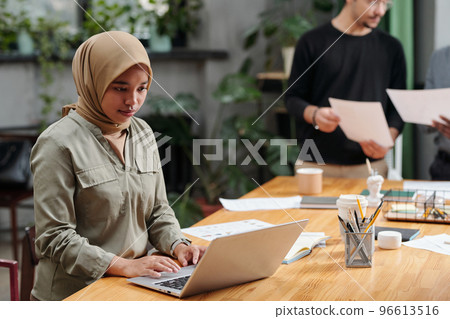 Young serious businesswoman in hijab looking at laptop screen Young serious businesswoman in hijab looking at laptop screen 96613516