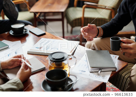 Hands of young businessman with cup of tea talking to colleagues 96613633
