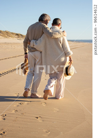 Senior couple walking barefoot on wet sand at seashore 96614612