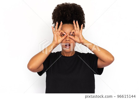 Portrait of surprised young woman making binoculars gesture 96615144