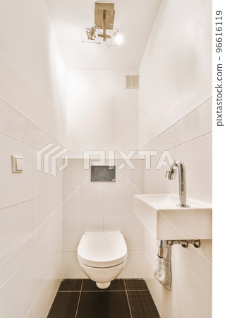 Interior of narrow restroom with sink and wall hung toilet with white walls and checkered floor 96616119