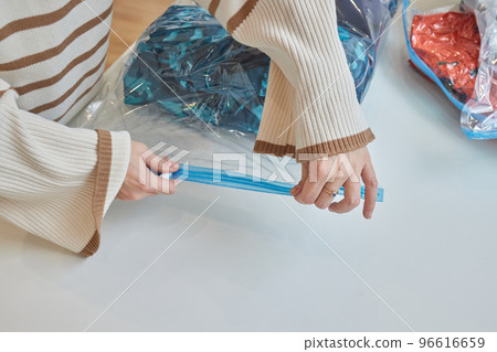 The girl pumps out air with a vacuum cleaner from a vacuum bag with clothes. The concept of storage and transportation of clothing, things. Space saving seal bag. The girl pumps out air with a vacuum cleaner from a vacuum bag with clothes. The concept of storage and transportation of clothing, things. Space saving seal bag. 96616659