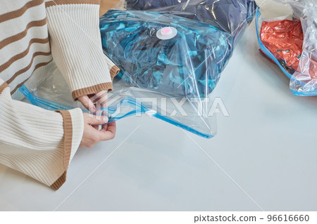 The girl pumps out air with a vacuum cleaner from a vacuum bag with clothes. The concept of storage and transportation of clothing, things. Space saving seal bag. The girl pumps out air with a vacuum cleaner from a vacuum bag with clothes. The concept of storage and transportation of clothing, things. Space saving seal bag. 96616660