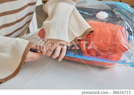 The girl pumps out air with a vacuum cleaner from a vacuum bag with clothes. The concept of storage and transportation of clothing, things. Space saving seal bag. 96616731