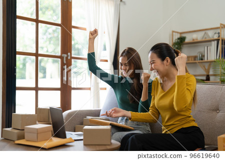 Two Young Asian women are happy and excited after a new order from SME customer, commercial checking, online marketing, Entrepreneur packing boxes, SME sellers, and freelance online sales concept 96619640