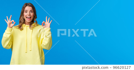 Cheerful blond female friend encourage you, praise girlfriend making good job, showing okay gestures and smiling, rooting for person during match, leave positive review, blue background 96620127