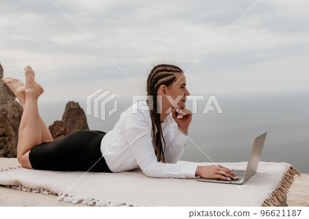 Silhouette of laptop and cup on the beach over sea sunset. Sparkling sea water on background. Freelancer, blogger working on notebook on the beach. 96621187