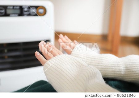 A woman who warms up with a fan heater 96621846