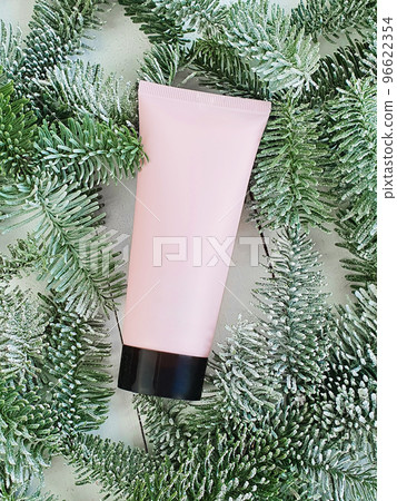 Mockup pink squeeze bottle cosmetic tube with screw black cap and snowy branches of Christmas fir tree on white wood background. Body cream, gel, skincare, moisturizer. Front top view, blank tube. 96622354