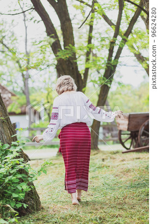 beautiful peasant woman in embroidered clothes walks around the yard 96624280