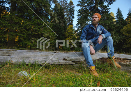 man with a beard sits on a log in the forest. Adventure, travel, tourism and vacation concept - smiling man relaxing in the forest 96624496