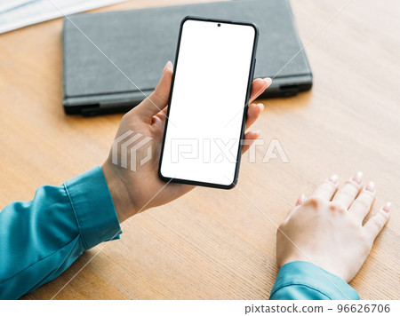 Online conference. Office woman. Digital mockup. Female hands holding smartphone with blank screen sitting desk in light room interior. Online conference. Office woman. Digital mockup. Female hands holding smartphone with blank screen sitting desk in light room interior. 96626706