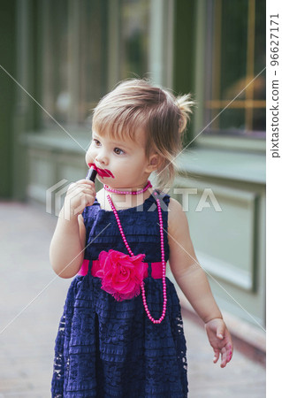 Adorable baby in a dress paints lips with lipstick 96627171