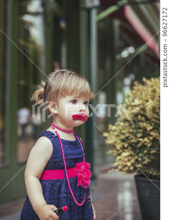 Adorable baby in a dress paints lips with lipstick Adorable baby in a dress paints lips with lipstick 96627172