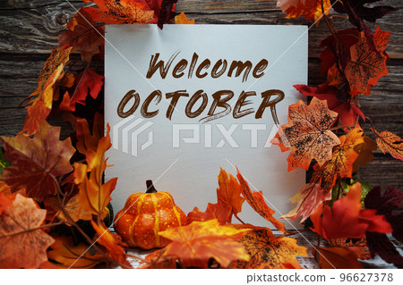 Welcome October text message with autumn maple leaves and pumpkins on wooden background 96627378