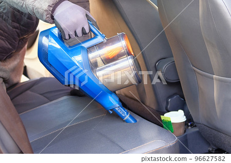 Vacuum cleaner in hands of driver. Cleaning of interior of the car with blue vacuum cleaner. Car textile seats is regular clean up. 96627582