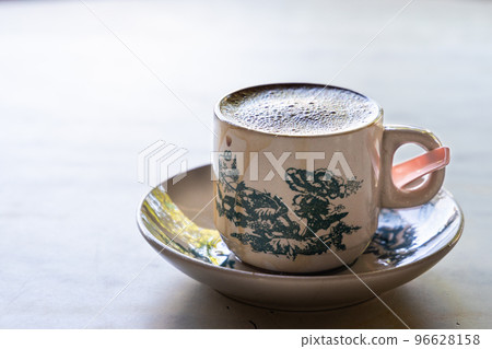 Aromatic frothy coffee served in traditional chinese cup and saucer in kopitiam against backlight Aromatic frothy coffee served in traditional chinese cup and saucer in kopitiam against backlight 96628158