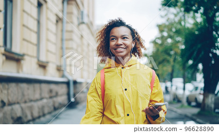 Carefree African American student is walking, listening to music through earphones during leisure time. Modern technology, youth culture, cities and people concept. Carefree African American student is walking, listening to music through earphones during leisure time. Modern technology, youth culture, cities and people concept. 96628890