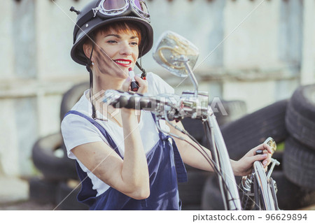 Girl auto mechanic in helmet looks in motorcycle mirror and paint lips Girl auto mechanic in helmet looks in motorcycle mirror and paint lips 96629894