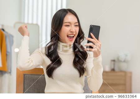 Millennial asian young woman looking mobile phone laughing with good news or discount voucher for shopping online at home.Happy and cheerful woman looking on cellphone app read message feel excited 96633364