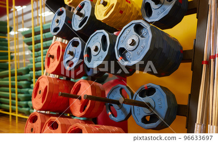Dumbbells of different sizes. dumbbells in the fitness room. Dumbbells of orange, green and yellow. Rack with metal pancakes of different weights. 96633697