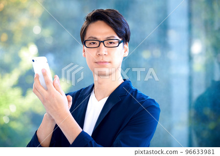 A young businessman in a suit operating a smartphone at the entrance 96633981