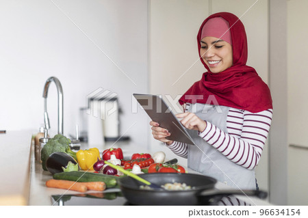 Beautiful middle eastern woman cooking at home, reading culinary blog Beautiful middle eastern woman cooking at home, reading culinary blog 96634154