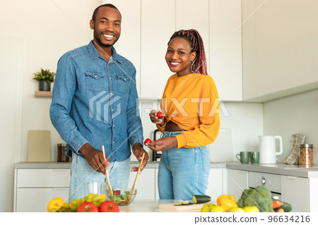 Positive african american man and woman cooking together at home, making delicious vegetable salad, kitchen interior 96634216