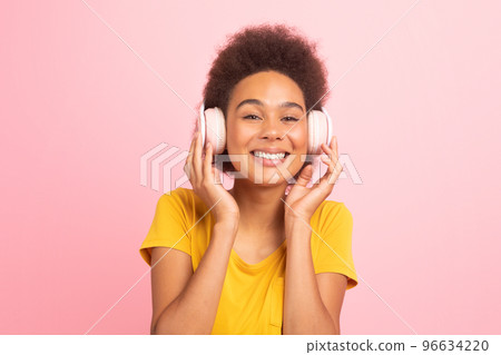 Smiling millennial african american curly female student in casual and wireless headphones, enjoy music 96634220