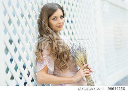 Portrait of a beautiful girl with flowing curly hair, smiling, looking at the camera on the street. Walking around the city, with a bouquet of lavender in your hands. High quality photo Portrait of a beautiful girl with flowing curly hair, smiling, looking at the camera on the street. Walking around the city, with a bouquet of lavender in your hands. High quality photo 96634258