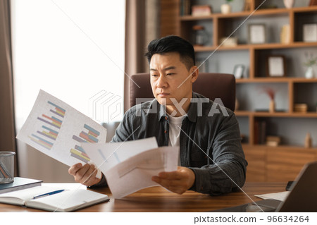 Busy serious concentrated middle aged asian man reads documents, think about project in home office interior Busy serious concentrated middle aged asian man reads documents, think about project in home office interior 96634264