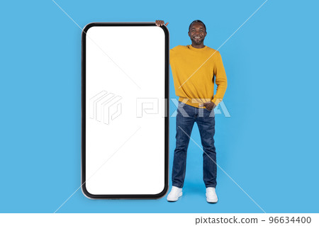 Cheerful cool black man posing by huge smartphone on blue Cheerful cool black man posing by huge smartphone on blue 96634400