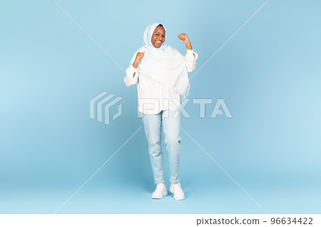 Happy black woman in hijab celebrating success, lady cheering luck with clenched fists, blue background, full length Happy black woman in hijab celebrating success, lady cheering luck with clenched fists, blue background, full length 96634422
