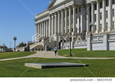 A lone man walks away in front of the Capitol building on a sunny day. A lone man walks away in front of the Capitol building on a sunny day. 96634505
