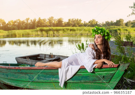 The nymph with long dark hair in a white vintage dress sitting in a boat in the middle of the river. 96635187