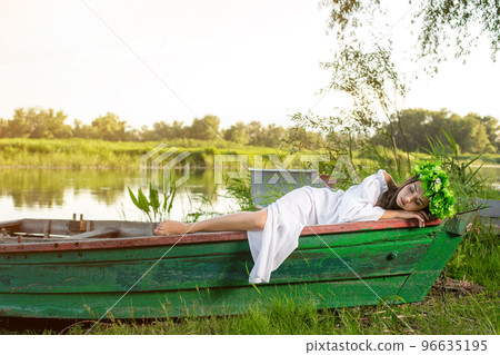 The nymph with long dark hair in a white vintage dress sitting in a boat in the middle of the river. The nymph with long dark hair in a white vintage dress sitting in a boat in the middle of the river. 96635195