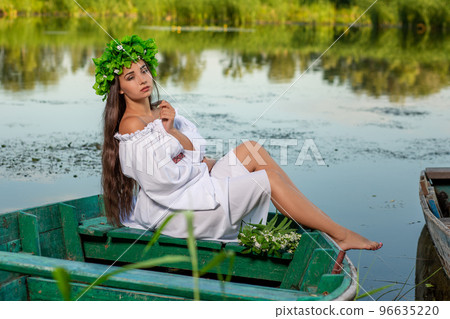 The nymph with long dark hair in a white vintage dress sitting in a boat in the middle of the river. 96635220