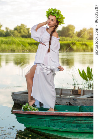 Young sexy woman on boat at sunset. The girl has a flower wreath on her head, relaxing and sailing on river. Fantasy art photography. Young sexy woman on boat at sunset. The girl has a flower wreath on her head, relaxing and sailing on river. Fantasy art photography. 96635287
