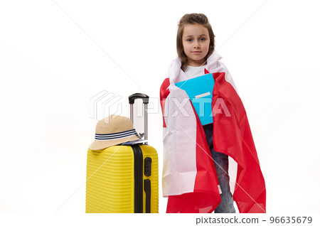 Happy first grader, Caucasian little child girl wrapping in Canadian flag, holding a copybook, posing with suitcase over white background. Concept of travelling to Canada for study. Language courses Happy first grader, Caucasian little child girl wrapping in Canadian flag, holding a copybook, posing with suitcase over white background. Concept of travelling to Canada for study. Language courses 96635679