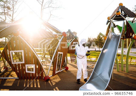 Man wearing protective suit disinfecting the playground in the sun with spray. Covid -19. Cleaning. Man wearing protective suit disinfecting the playground in the sun with spray. Covid -19. Cleaning. 96635746
